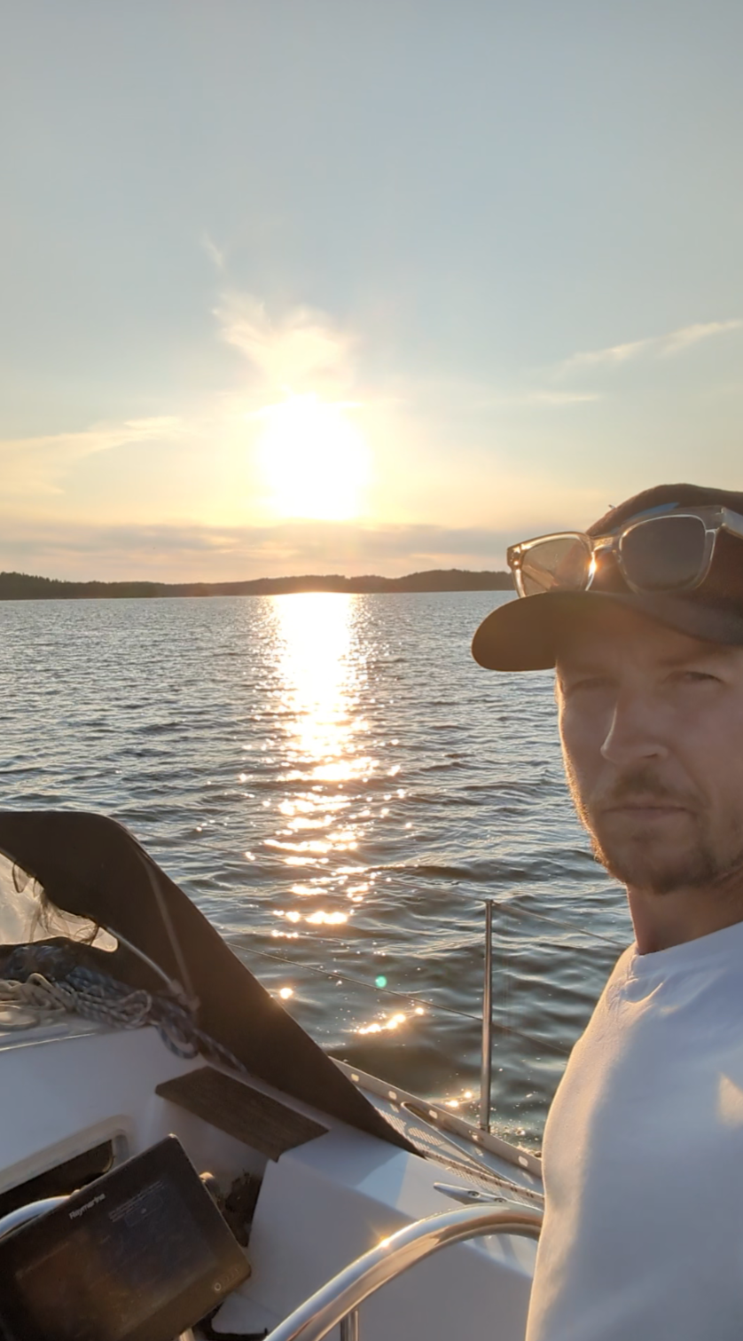 Kippari purjeveneen ruorissa auringonlaskussa